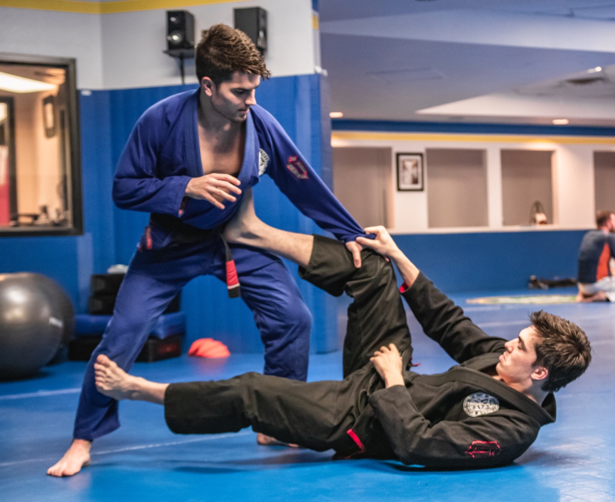 John, in a blue gi, working a guard pass against his brother, Jean, in a black gi